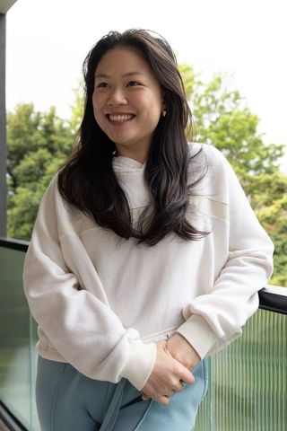 Asian woman smiling on balcony wearing white hoodie and gold hoop earrings, lifestyle
