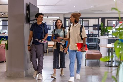 Diverse college students walking through modern campus lounge holding notebooks and tablet