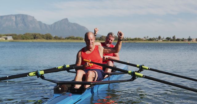 Two senior men kayaking on a clear lake with a mountain backdrop, celebrating their activity. Ideal for use in promotions related to active aging, outdoor sports, fitness regimens for older adults, adventure travel brochures, and healthy lifestyle guides.