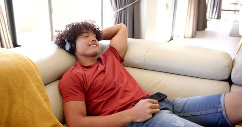 Young Adult Relaxing With Headphones on Sofa Holding Smartphone
