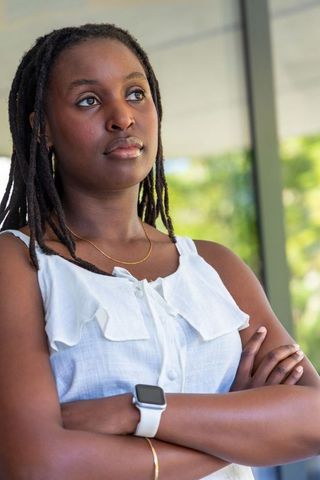 African woman standing with arms crossed gazing upward in white blouse, smartwatch and gold jewelry