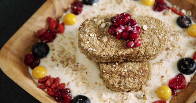 A wooden plate holds a nutritious serving of oatmeal cookies garnished with pomegranate seeds and assorted berries, with copy space. Fresh and dried fruits add a colorful contrast to the wholesome, fiber-rich snack.