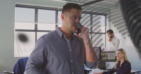 Businessman talking on smartphone in modern open-plan office with team collaborating