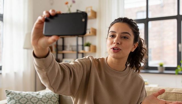Young woman recording lifestyle vlog with smartphone in cozy living room apartment