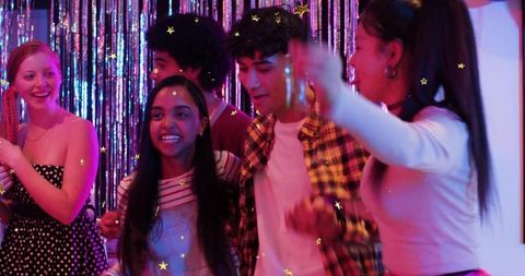 Dancing young friends celebrating at retro tinsel party with colorful lighting and confetti