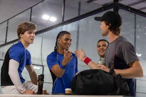 Multiethnic male teammates chatting and high-fiving on indoor glass court bench