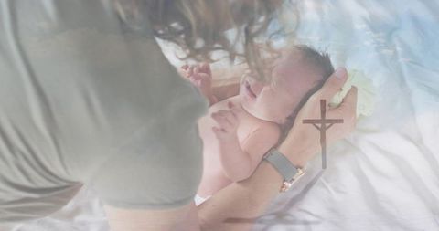 Mother cradling newborn with cross overlay, soft double exposure conveying faith and bonding