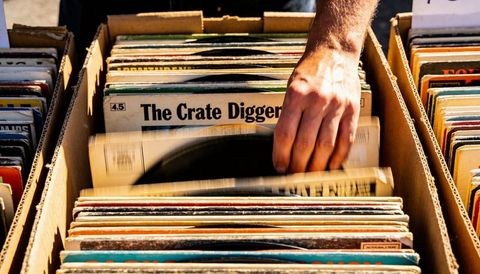 Sunlit hand flipping vintage vinyl in crates at outdoor record market with motion blur
