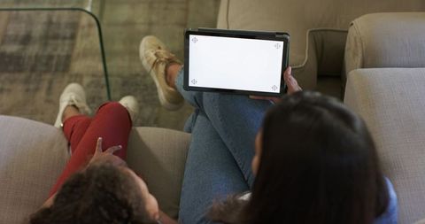 Parent and Child Relaxing on Sofa Sharing Tablet with Blank Screen for App Mockups