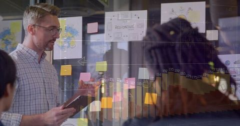 Creative team collaborating at glass wall with sticky notes and interactive data charts