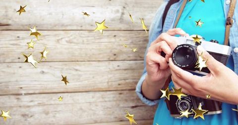 Holding vintage slr by rustic wooden wall with golden star overlay, nostalgic portrait