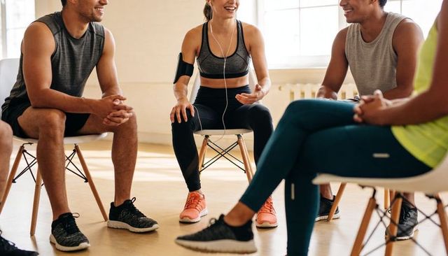 Group chatting after workout in sunlit studio woman gesturing with smartphone armband