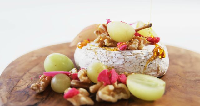 Close-up of Brie cheese garnished with fresh green grapes, walnuts, pink pickles, and a drizzle of honey on a wooden board. Perfect for gourmet food blogs, culinary presentations, menu designs, or organic food promotions. Emphasizes gourmet dining and high-quality ingredients.