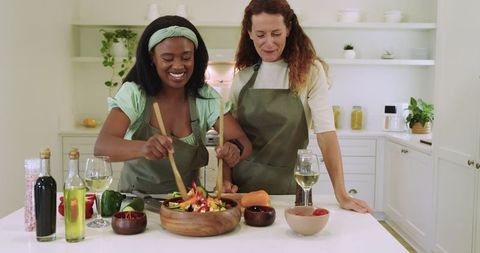 Diverse friends cooking together in modern kitchen with salad and wine
