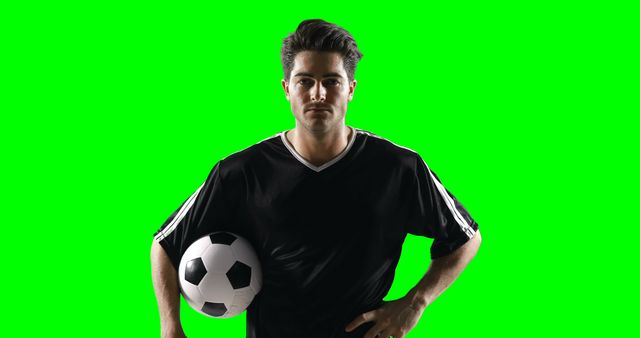 Soccer player standing confidently with ball against green background. Perfect for sports promotions, advertising, football team branding, and educational materials about soccer training.