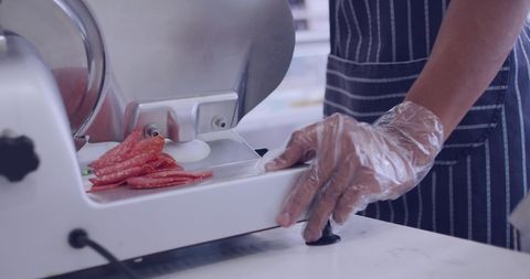 Deli chef slicing salami with professional meat slicer