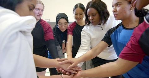 Diverse female athletes uniting in team huddle, stacking hands around coach for motivation