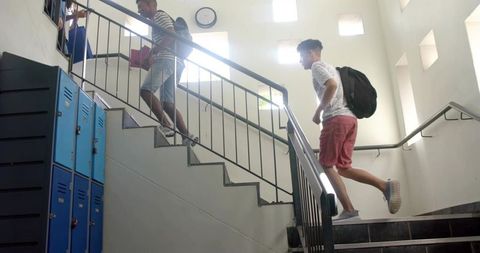 Students Climbing School Staircase Carrying Backpacks beside Lockers and Clock