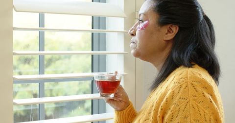 Woman enjoying herbal tea with under-eye patches for relaxation
