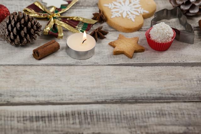 Christmas cookies and a tealight candle on a wooden plank create a cozy and festive atmosphere. Ideal for holiday-themed designs, greeting cards, social media posts, and seasonal advertisements.