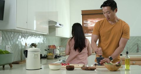 Couple cooking together in contemporary kitchen, man grinding herbs with mortar and pestle