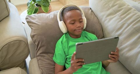 African american boy relaxing on couch using tablet and white headphones at home