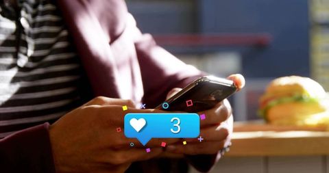 Man checking heart notification on smartphone in casual cafe with burger