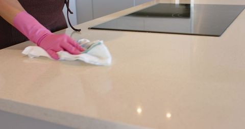 Pink-gloved hand cleaning quartz countertop with striped rag beside black induction hob