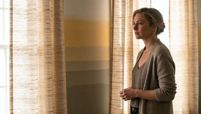 Contemplative woman by sheer curtains, warm natural light, cozy cardigan, textured wall