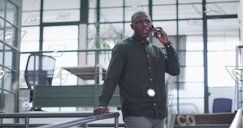 Young professional talking on smartphone leaning on modern office railing with ar graphics