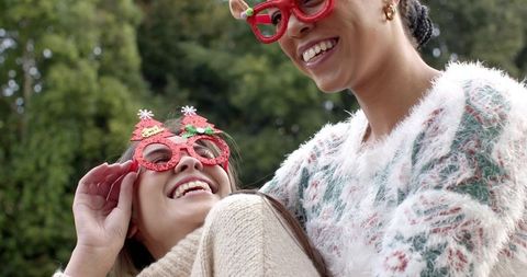 Diverse women laughing in red glitter holiday glasses wearing cozy knit sweaters outdoors