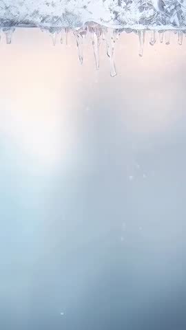 Icicles hanging from roof eave with drifting snowflakes and peach glow vertical video