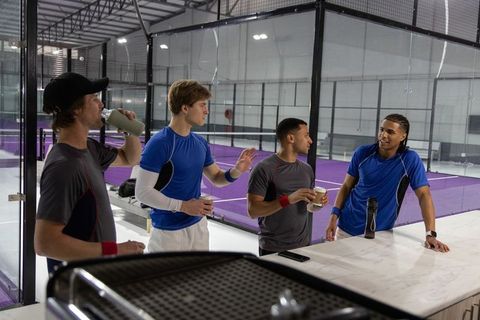 Multicultural male athletes chatting, drinking and resting at indoor padel courts