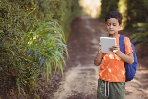 Boy exploring nature trail with tablet and backpack
