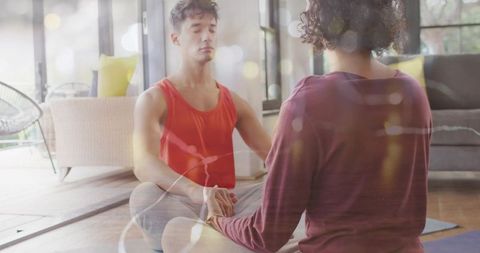 Couple meditating together holding hands on yoga mats in sunlit living room