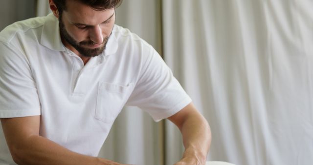 Male massage therapist in a white shirt, performing a massage. Ideal for content related to wellness, healthcare, physical therapy, spa treatments, and self-care routines. Can be used in marketing materials for spa services, wellness blogs, or healthcare websites.