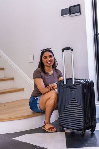 Young african woman sitting on foyer stairs with suitcase, smiling, casual summer travel lifestyle