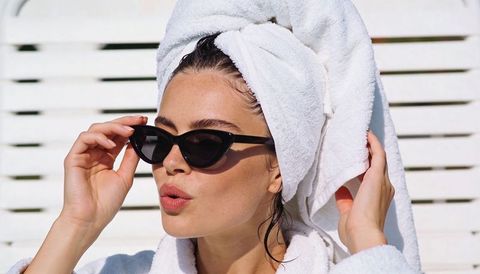 Sunlit glamour: woman in towel turban adjusting cat-eye sunglasses at poolside