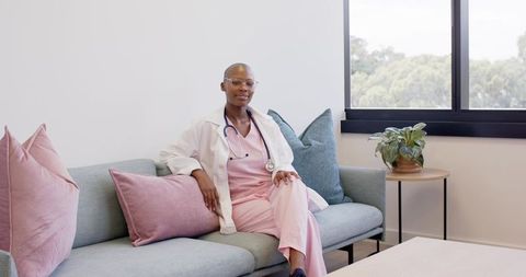 Doctor relaxing on clinic sofa wearing pink scrubs and white coat with stethoscope