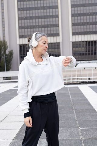 Mature woman checking smartwatch on rooftop terrace while listening with headphones