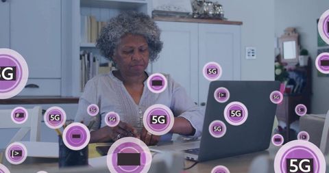 Senior woman working on laptop at kitchen table surrounded by 5g connectivity icons