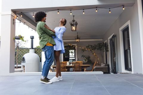 African american couple dancing and laughing on covered patio with string lights