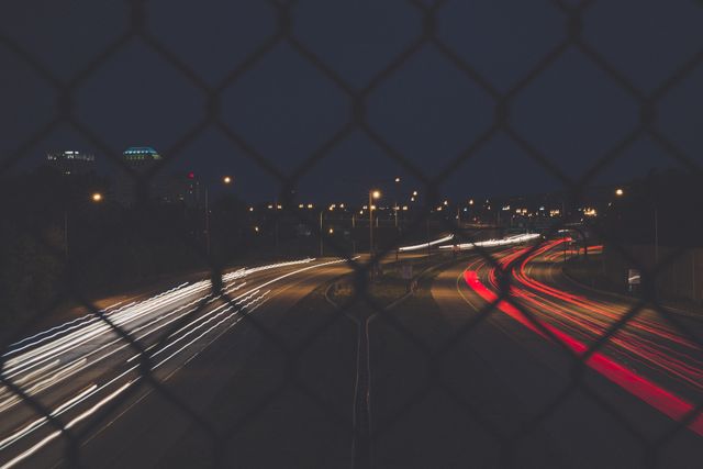 Blurry City Highway with Traffic Light Trails at Night through Chain Link Fence - Download Free Stock Photos Pikwizard.com