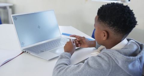 Teen student typing on laptop in classroom wearing hoodie and headphones, learning