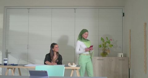 Diverse coworkers collaborating in minimal office, woman in headscarf checking phone