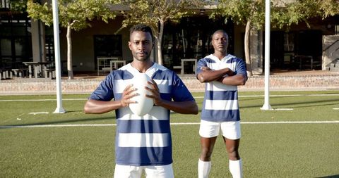 Rugby Players Holding Ball on Grass Field in Striped Jerseys