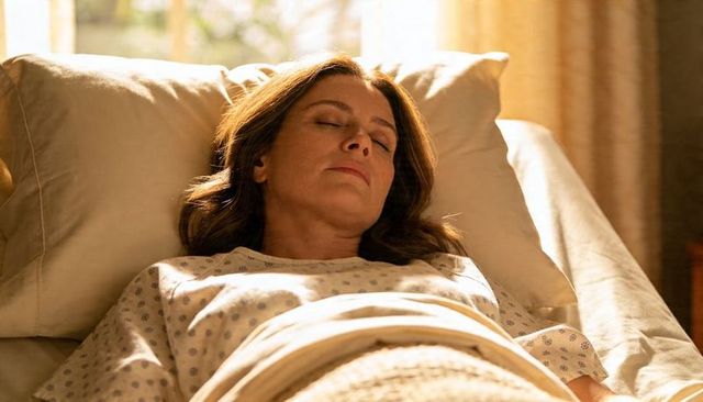 Middle-aged woman resting peacefully on bed in warm sunlit bedroom, serene recovery