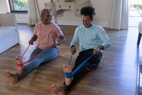 Senior woman and man exercising with resistance bands on hardwood floor in living room