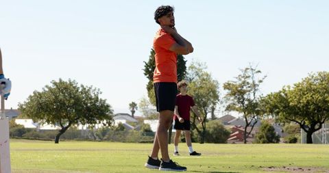 Young athlete stretching neck on sunny sports field wearing orange shirt
