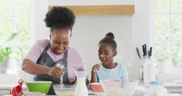 Grandmother and young girl baking together in bright modern kitchen, engaging in a joyful bonding activity. Ideal for use in family lifestyle, cooking products, and intergenerational bonding concepts. Perfect for content focused on family traditions, home baking recipes, and togetherness themes.